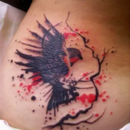 Tatuaż przedstawiający lecącego ptaka z elementami drzewa i czerwonymi plamami, wykonany na skórze w okolicy biodra.