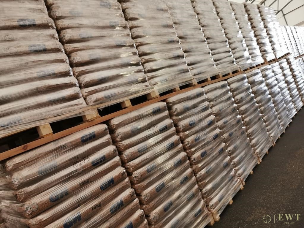 Magazyn pelletu: Rzędy palet z workami pelletu owiniętymi folią stretch, widoczne oznaczenia 10kg i logo producenta na workach.