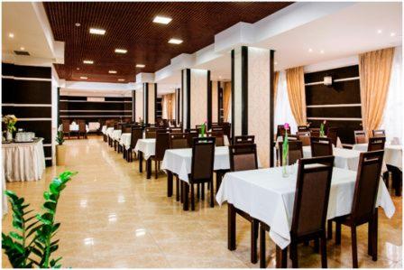 Sala restauracyjna w hotelu z rzędami nakrytych stołów, brązowymi krzesłami i dekoracyjnymi kolumnami.