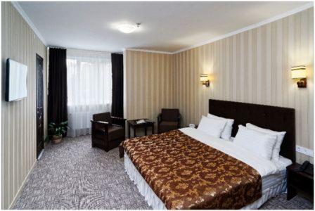 Pokój hotelowy z brązową narzutą w kwiaty, tapetami w pionowe pasy, ciemnymi zasłonami i drewnianymi meblami.