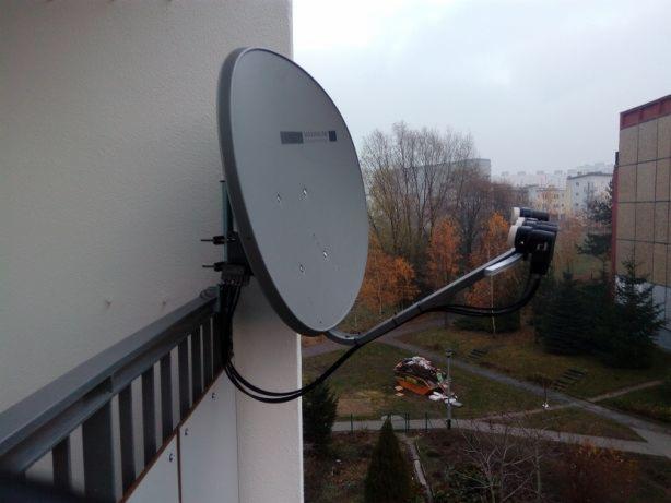 Szara antena satelitarna zamontowana na balkonie bloku mieszkalnego, widok na osiedle w jesiennej scenerii.