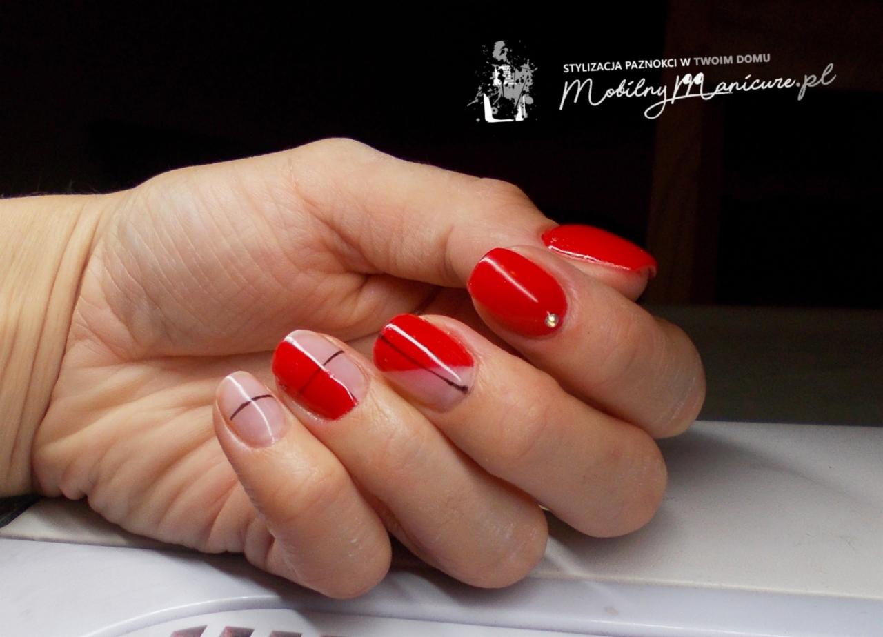 Dłoń z czerwonymi paznokciami, dwa z nich z geometrycznym wzorem: czerwona połowa oddzielona czarną linią od naturalnej płytki. Jeden paznokieć ozdobiony drobnym dżetem.