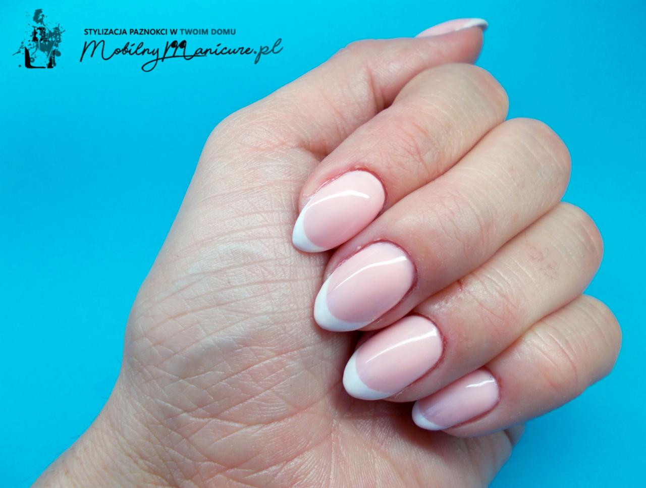 Delikatny french manicure na owalnych paznokciach, pastelowy róż z białą końcówką, na tle turkusowym.