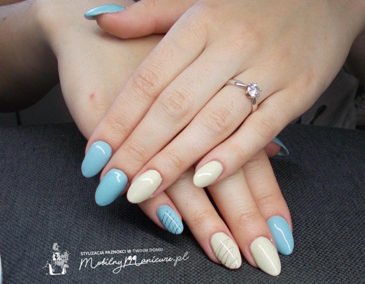 Dłonie kobiety z pomalowanymi paznokciami w odcieniach błękitu i kremowej bieli, jeden paznokieć z delikatnym geometrycznym wzorem, pierścionek z oczkiem na palcu serdecznym.