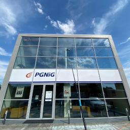 INMAGO Sp. z o.o., Sp. k. - Czyszczenie szklanej fasady budynku PGNIG z użyciem teleskopowego kija i myjki, widoczne smugi wody na szybach, błękitne niebo z chmurami odbija się w oknach.