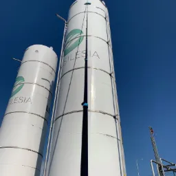 Czyszczenie przemysłowe wysokiego zbiornika z logo 'Silesia' za pomocą teleskopowej lancy myjącej pod kątem od dołu, widoczne zacieki na powierzchni zbiornika.