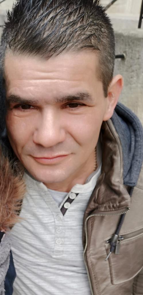 Portret mężczyzny w skórzanej kurtce, z bliska, z delikatnym uśmiechem, na rozmytym tle. Widoczna faktura skóry kurtki i detale ubrania.