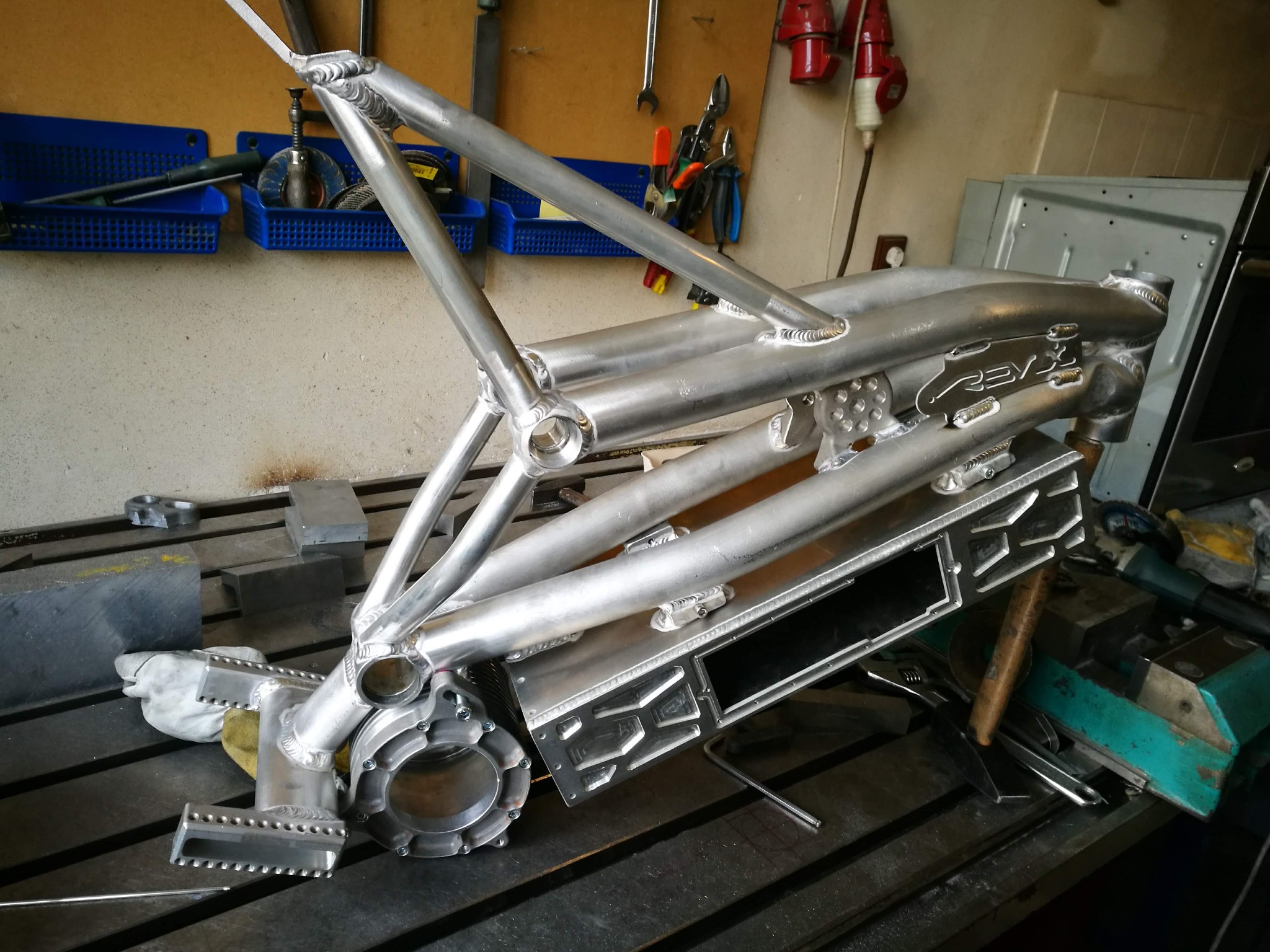 Aluminiowa rama pojazdu po spawaniu, widoczne precyzyjne spawy i detale konstrukcyjne, tło warsztatowe z narzędziami.