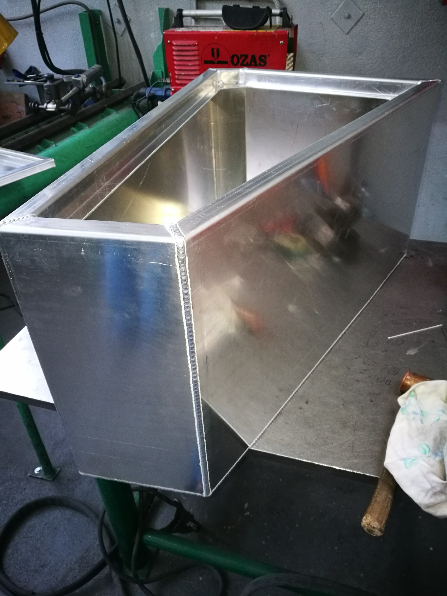 Spawana aluminiowa skrzynka z widocznymi spawami, wykonana w Jarnołtówku, na tle stołu warsztatowego i spawarki marki LOZAS.