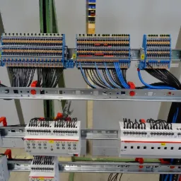 Rozdzielnica elektryczna z licznymi przewodami, listwami zaciskowymi i modułami sterującymi ABB, zamontowana na metalowej konstrukcji nośnej wewnątrz budynku.