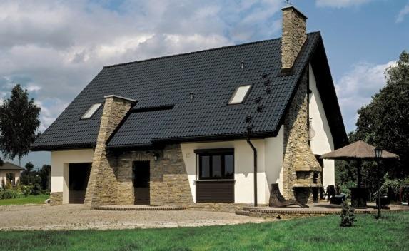 Dom jednorodzinny z ciemną dachówką ceramiczną, kamienną elewacją i kominami, widoczne okna dachowe i zadbany trawnik.