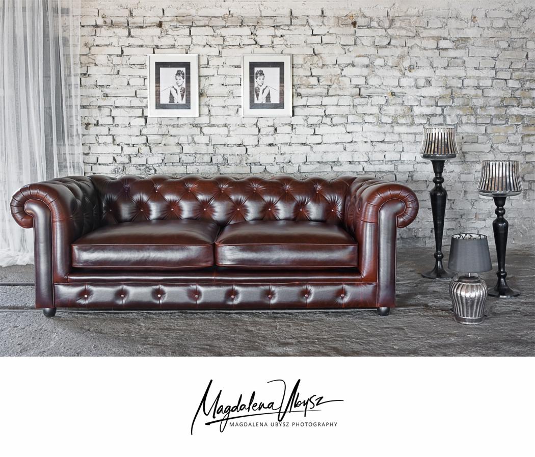 Brązowa skórzana sofa Chesterfield na tle białej ceglanej ściany z dwoma czarno-białymi portretami i trzema lampami