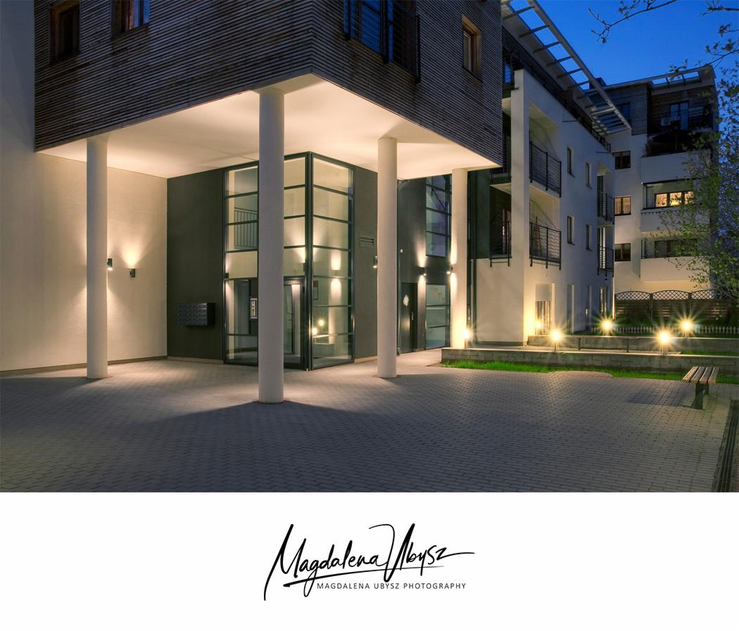 Elegancki budynek mieszkalny z nowoczesnym wejściem, oświetlonym lampami punktowymi, sfotografowany o zmierzchu z niskiego kąta.