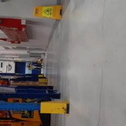 Pomiar wewnątrz magazynu, widoczny pracownik z narzędziami pomiarowymi, regały magazynowe i znak ostrzegawczy 'AGV STOP'.