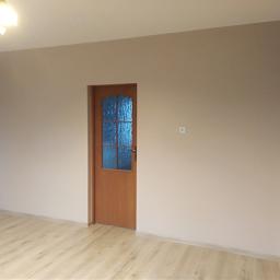 Łukasz Nawrocki - Pomalowane na beżowo wnętrze z drewnianymi drzwiami z szybą i panelami podłogowymi, widoczny włącznik na ścianie.