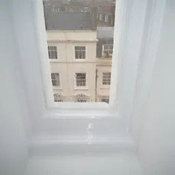 Świeżo pomalowane na biało wnętrze okna dachowego z widokiem na budynki miejskie w pochmurny dzień.