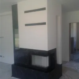 Nowoczesny kominek obudowany czarnym marmurem z białymi żyłami, w minimalistycznym wnętrzu z dwiema poziomymi wnękami nad paleniskiem.