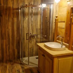 Drewniana łazienka w stylu rustykalnym z kabiną prysznicową, umywalką nablatową i oświetleniem punktowym, wykończona w ciepłych odcieniach brązu i beżu.