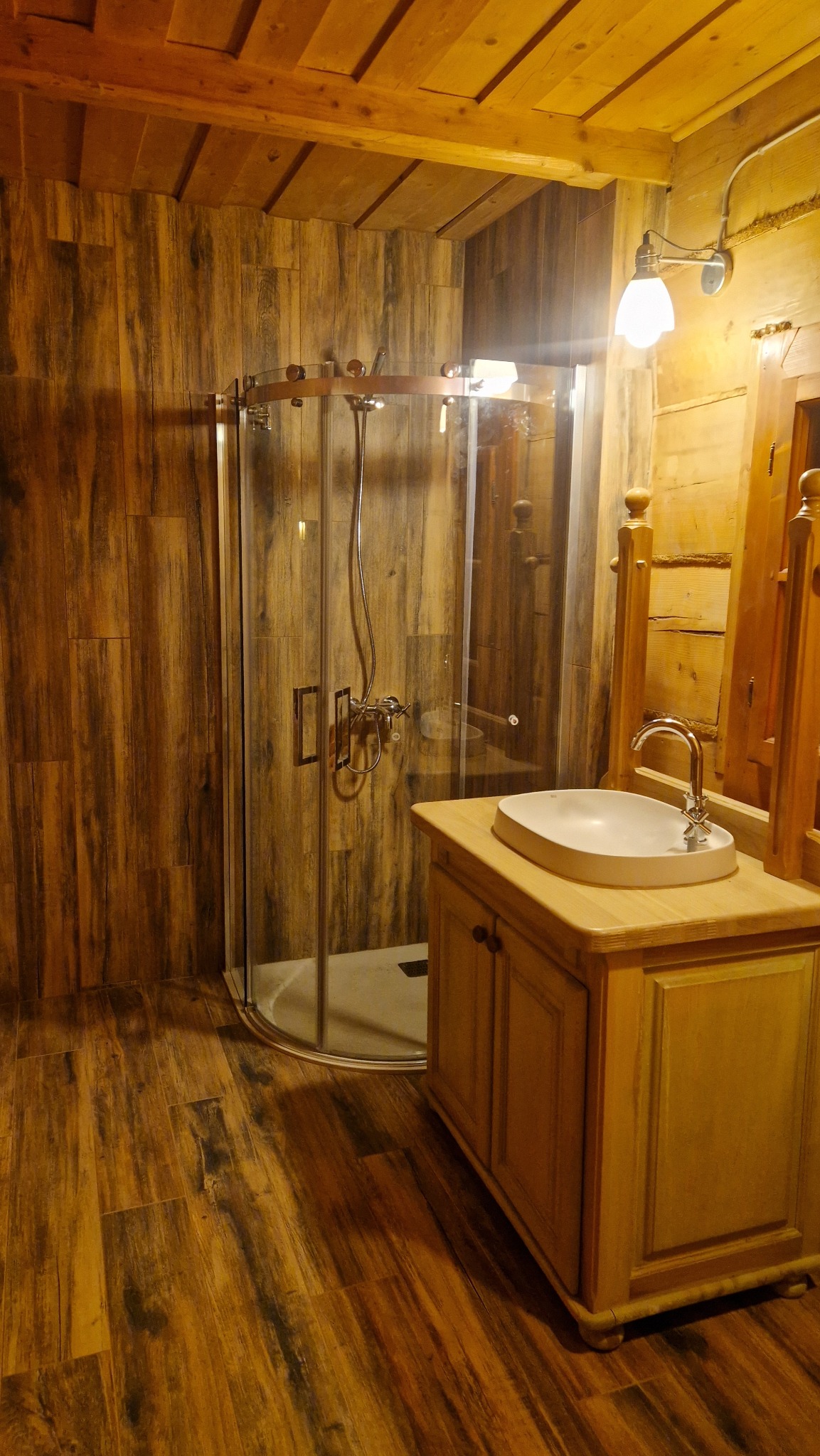 Drewniana łazienka w stylu rustykalnym z kabiną prysznicową, umywalką nablatową i oświetleniem punktowym, wykończona w ciepłych odcieniach brązu i beżu.