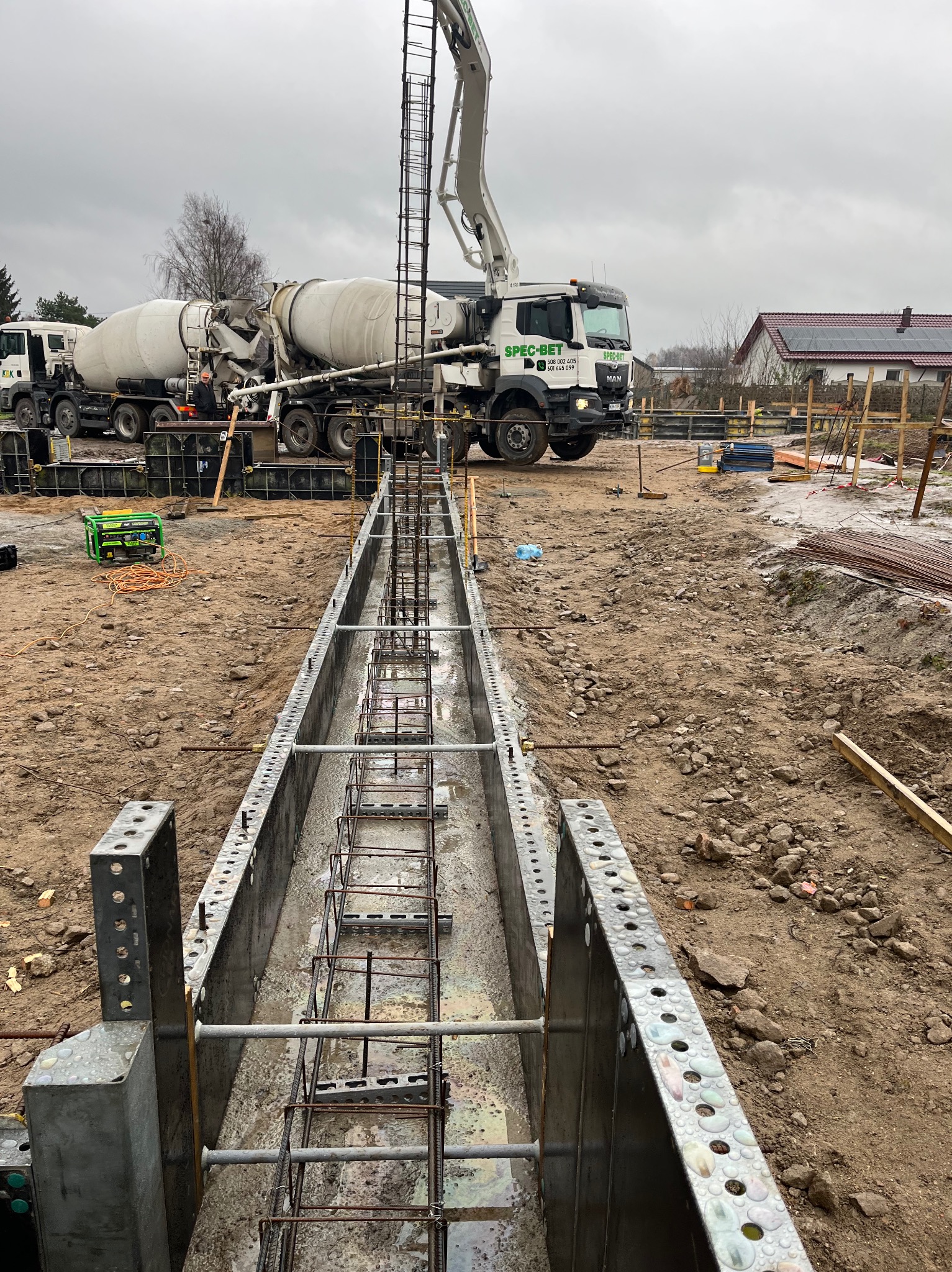 Przygotowanie fundamentów: szalunek zbrojony stalą, betonowozy SPEC-BET w tle, generator prądu na placu budowy.