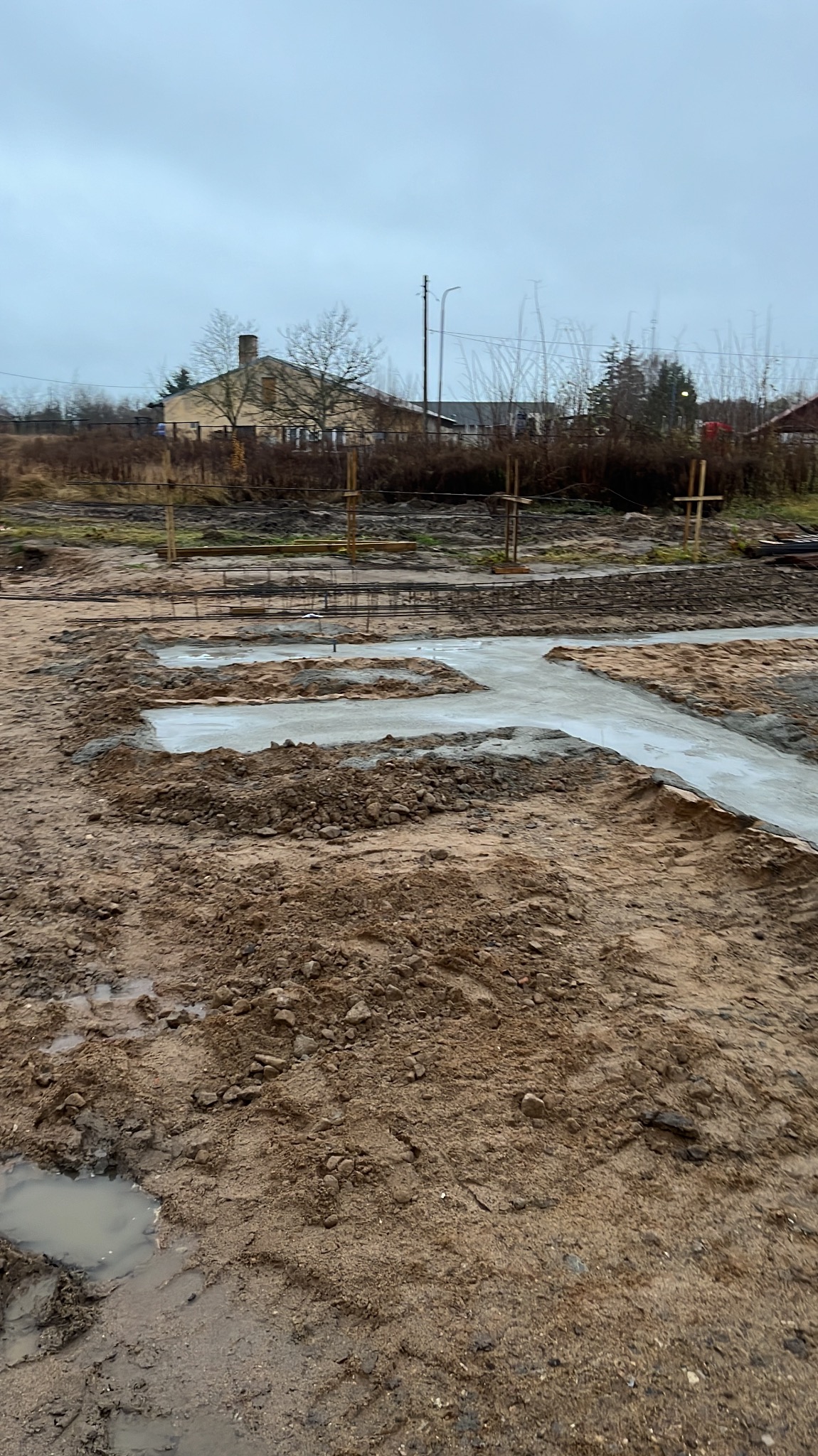 Wylany fundament pod budynek jednorodzinny na działce, widoczne zbrojenia i drewniane stemple, pochmurny dzień.