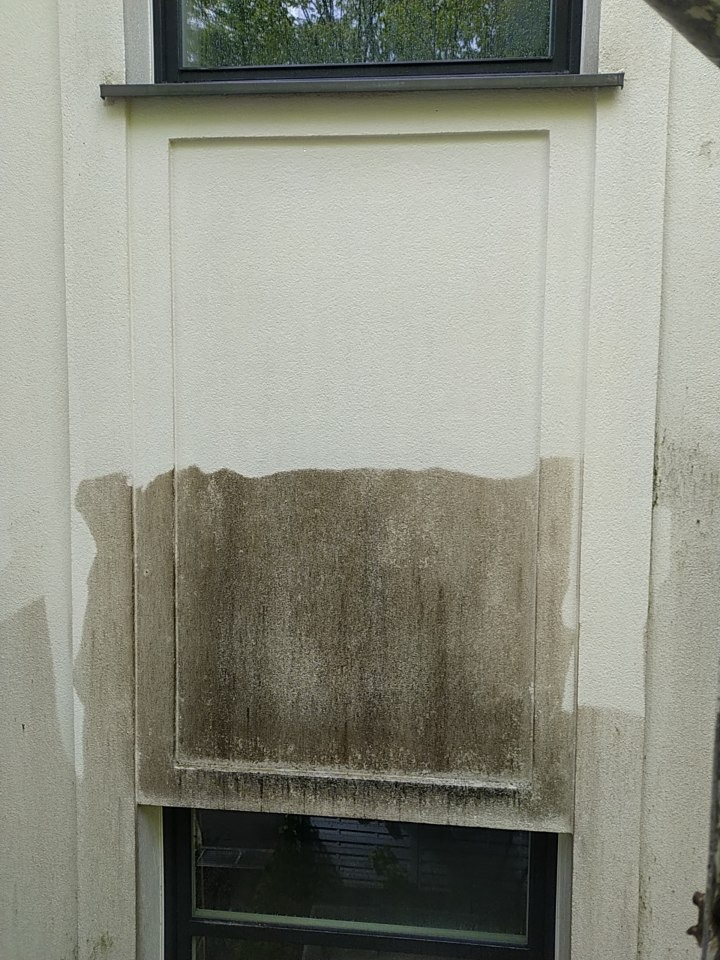 Zanieczyszczona, jasna elewacja budynku z widocznymi zaciekami i zabrudzeniami, z oknem na górze i na dole. Dolna część elewacji pokryta ciemnym nalotem.