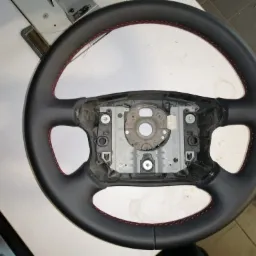 Obszyta czarną skórą kierownica samochodowa z czerwonym przeszyciem, widoczny metalowy szkielet kierownicy przed montażem w samochodzie.