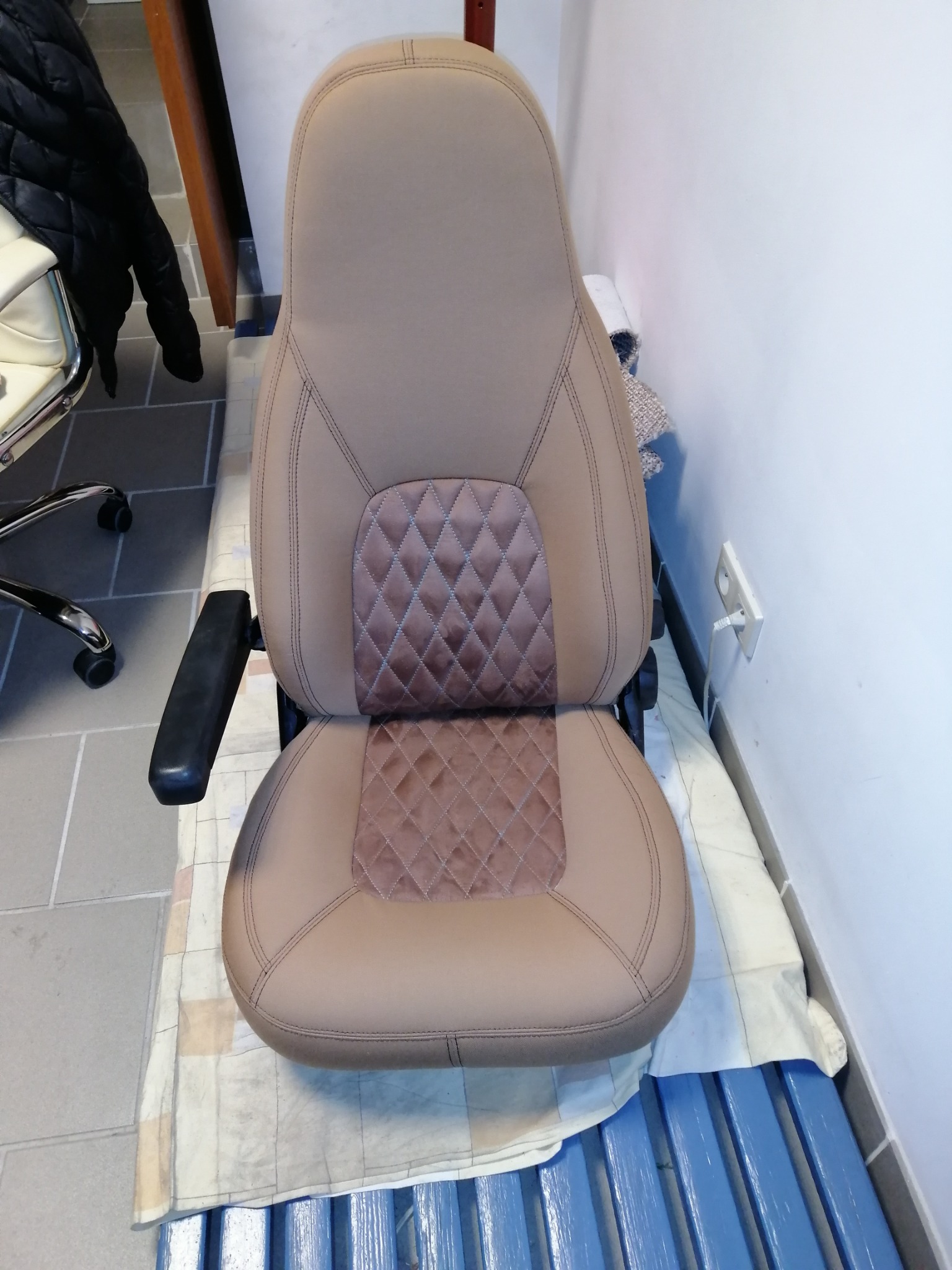 Odnowione, beżowe siedzenie samochodowe z brązowymi wstawkami w romby, ustawione na niebieskich deskach i poszewce, widok z przodu.