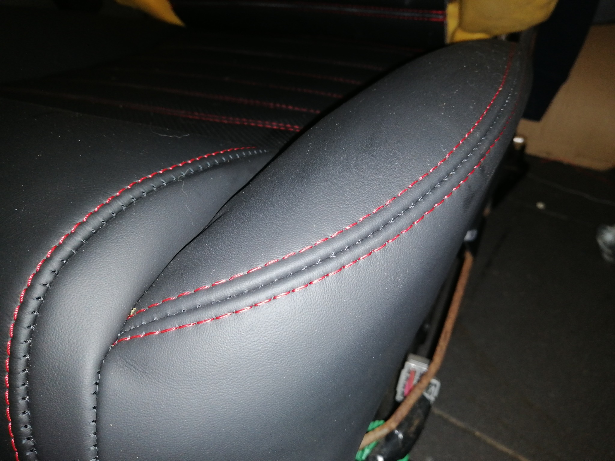 Fragment czarnego skórzanego fotela samochodowego z czerwonym szwem, widoczne detale tapicerki i szwów.
