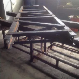 Stalowa konstrukcja szkieletowa z profili spawanych, widoczne spawy, surowy metal, szara podłoga warsztatowa, oświetlenie dzienne.