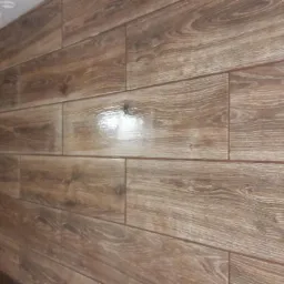 Ułożone, brązowe panele imitujące drewno na ścianie, z widoczną fugą, ułożone poziomo z perspektywicznym skrótem. Widoczne oświetlenie sufitowe.