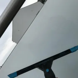 Szczotka do mycia okien 'Excelerator 2.0' z niebieskimi elementami gumowymi na tle szklanej elewacji budynku z widocznym fragmentem metalowej konstrukcji.