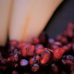 Makro zbliżenie na błyszczące, soczyste nasiona granatu z rozmytym tłem w odcieniach beżu i czerni.