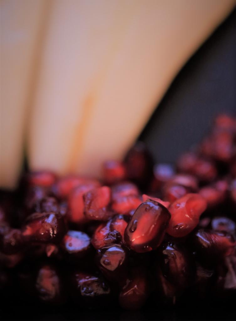 Makro zbliżenie na błyszczące, soczyste nasiona granatu z rozmytym tłem w odcieniach beżu i czerni.