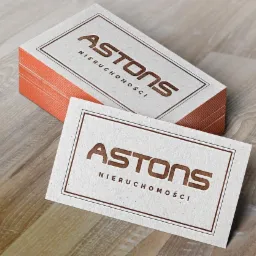 Stos wizytówek firmy ASTONS Nieruchomości na drewnianym tle, z widocznym brzegiem w kolorze łososiowym.
