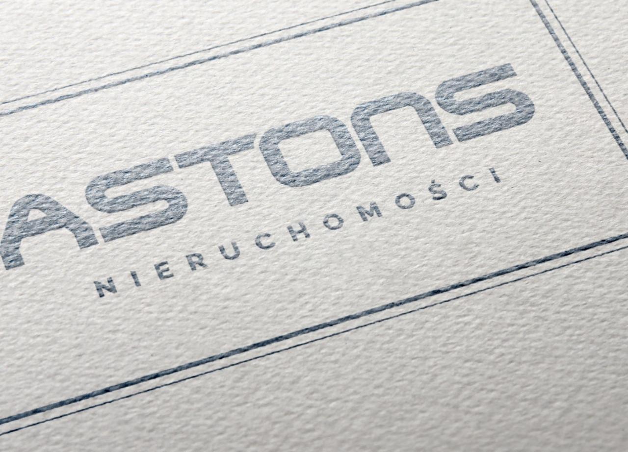Logo firmy ASTONS Nieruchomości wydrukowane w kolorze szarym na teksturowanym, kremowym papierze, z delikatnymi liniami obramowania.
