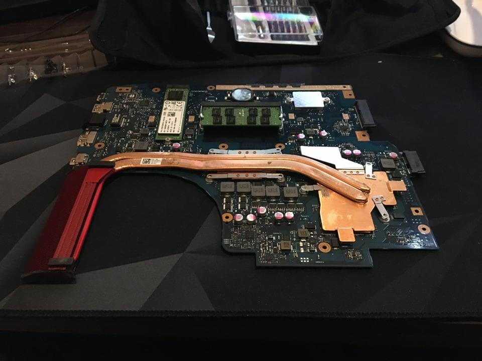 Płyta główna laptopa z miedzianym systemem chłodzenia, widoczne elementy elektroniczne i sloty pamięci RAM na czarnym podłożu.