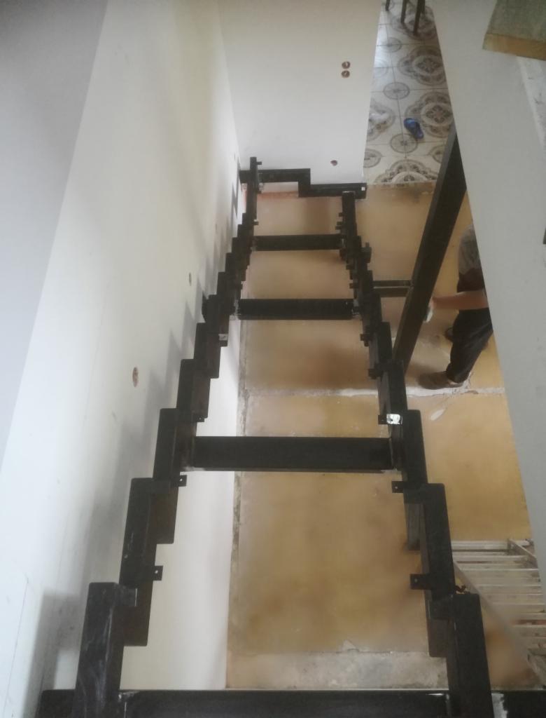 Konstrukcja stalowa schodów wewnętrznych w trakcie montażu, widoczne spawy i mocowania, surowe wnętrze w trakcie wykończenia.