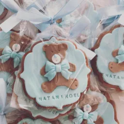 Pierniczki w kształcie misia z błękitną kokardą i napisem 'Natan i Noel' zapakowane w celofan z błękitną wstążką, jako upominki na uroczystość.