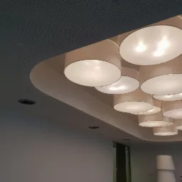 Nowoczesny sufit z perforacją i designerskimi, okrągłymi lampami w białych abażurach, tworzącymi kaskadową kompozycję.