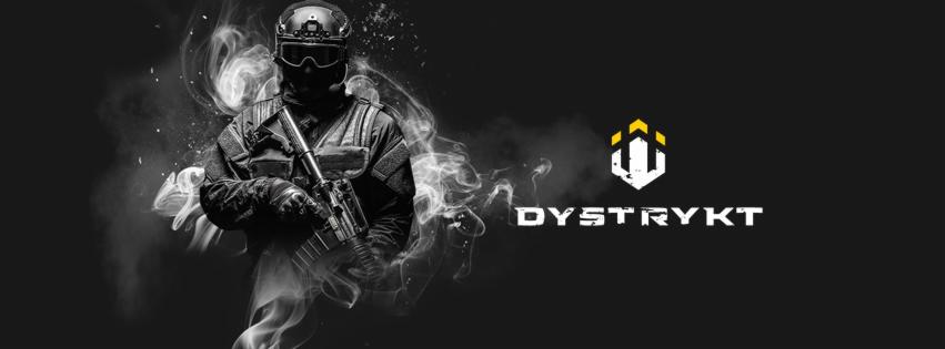 Mężczyzna w taktycznym stroju i hełmie, trzymający karabin, otoczony efektem dymu, obok logo i nazwa firmy 'DYSTRYKT' na czarnym tle.