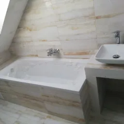Wykończona łazienka na poddaszu: wanna z baterią, obudowana płytkami imitującymi marmur, oraz umywalka nablatowa o kwadratowym kształcie, również na blacie z płytek. Wanna zabezpieczona folią...
