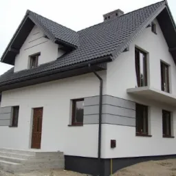 Dwupiętrowy dom z ciemną dachówką i jasną elewacją, z poziomymi szarymi pasami dekoracyjnymi, widok z boku na schody wejściowe.