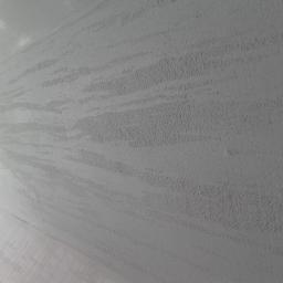 Tegulatoris - Świeżo pomalowana ściana z efektem dekoracyjnym, widoczne delikatne smugi i tekstura farby, jasny odcień bieli