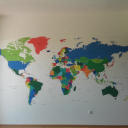 Tegulatoris - Ściana pomalowana na biało z naklejoną kolorową mapą świata, widoczny fragment drzwi po prawej stronie.