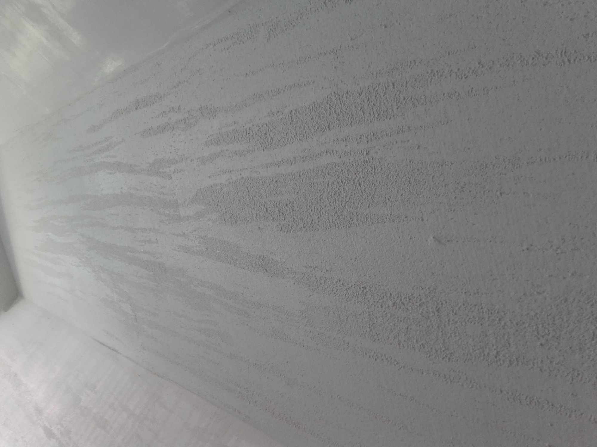 Świeżo pomalowana ściana z efektem dekoracyjnym, widoczne delikatne smugi i tekstura farby, jasny odcień bieli