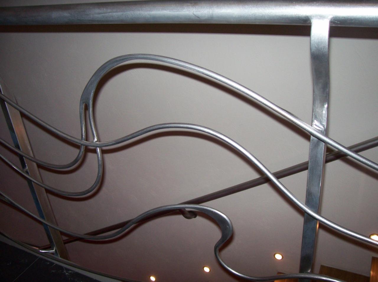 Nietypowa balustrada ze stali z giętymi prętami, widok od dołu, oświetlenie punktowe w tle.