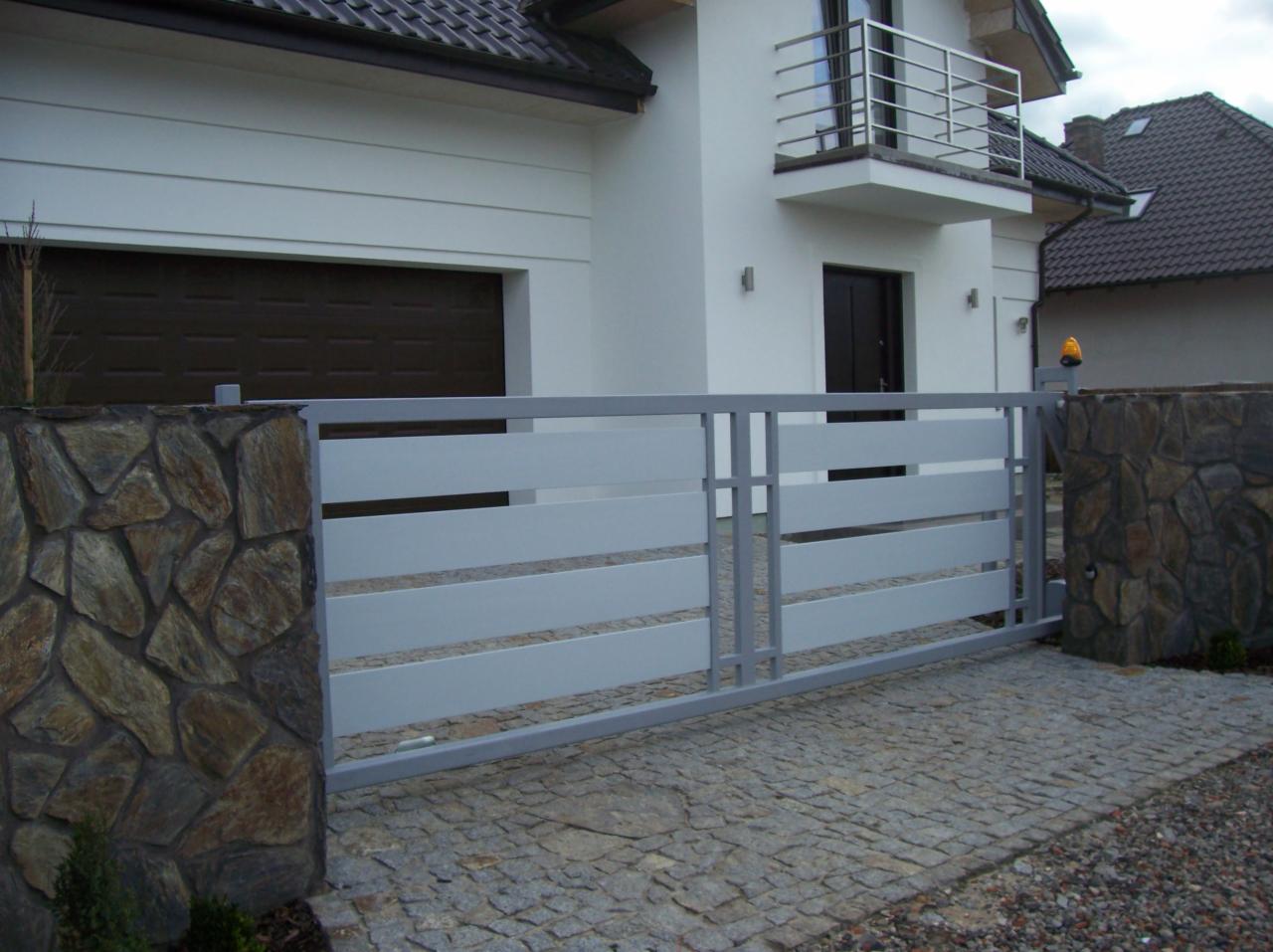 Nowoczesna brama posesyjna z poziomymi panelami w kolorze szarym, zamontowana w Swarzędzu, z kamiennymi słupkami i kostką brukową na podjeździe.