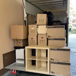Częściowo załadowany bus z kartonami Spaceo 57x35x40 cm i regałem z czterema przegródkami, przygotowany do transportu.