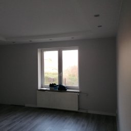 Projekt Venar - Pomalowane na szaro wnętrze pokoju z panelami podłogowymi, białym oknem i grzejnikiem. Na parapecie leżą buty i pudełko.